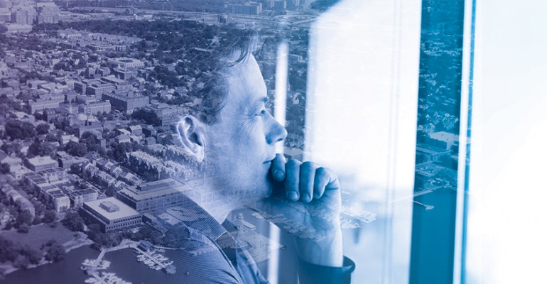 Profile of man looking out of a window, a city can be seen behind him